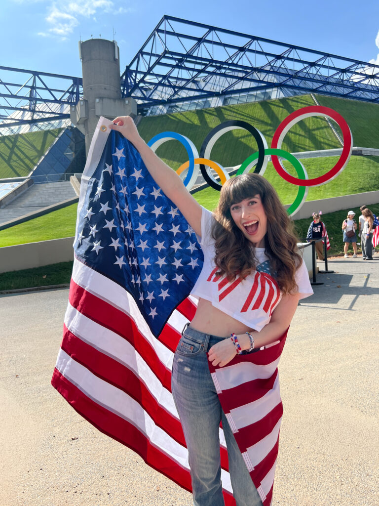 Bella posing with American flag and Olympic rings in background.