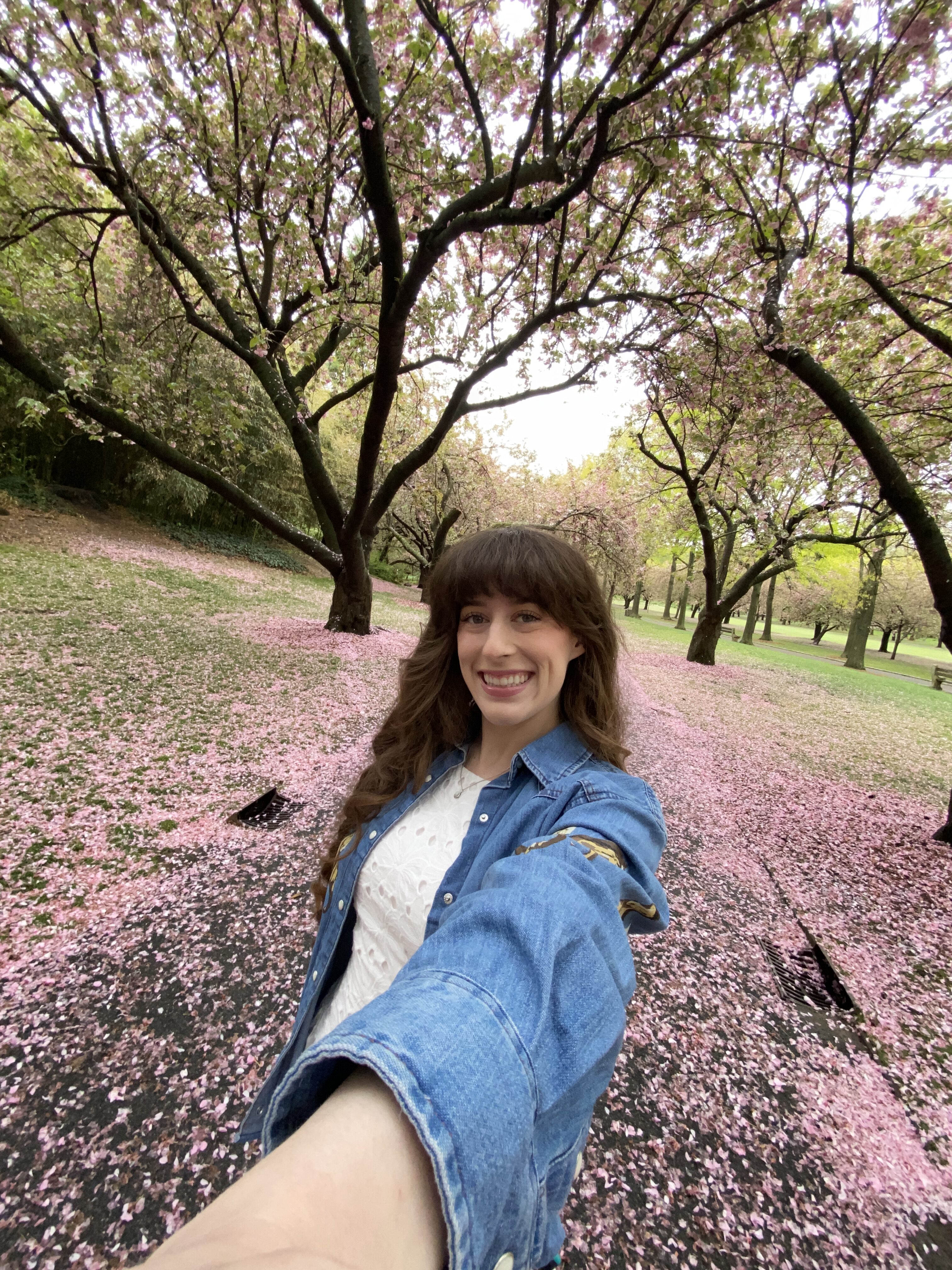 Bella smiling on a cherry blossom petal-covered walkway in the Brooklyn Botanic Gardens.