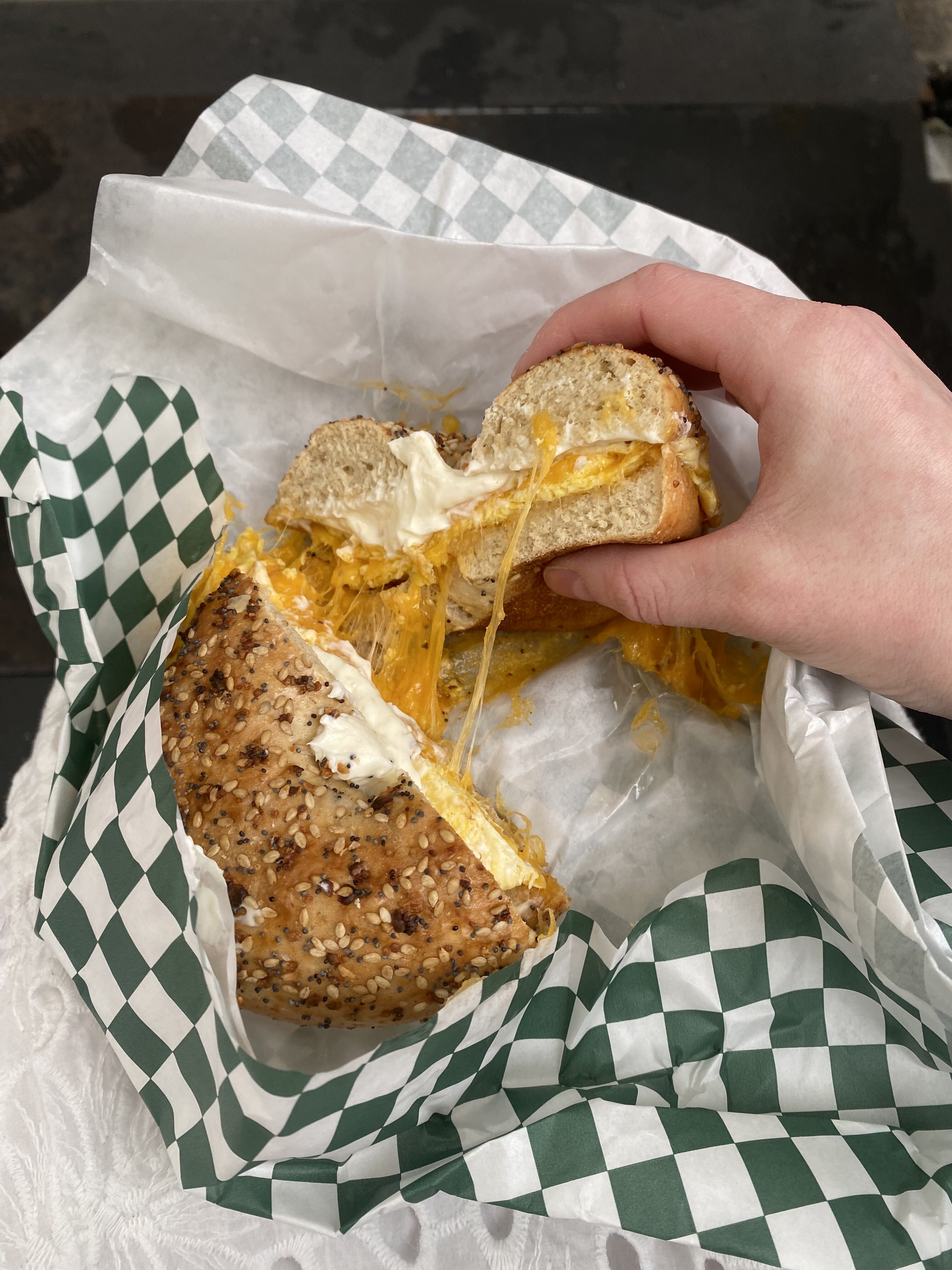 An egg and cheese bagel with cream cheese in a green/white checked paper from Leon's Bagel.