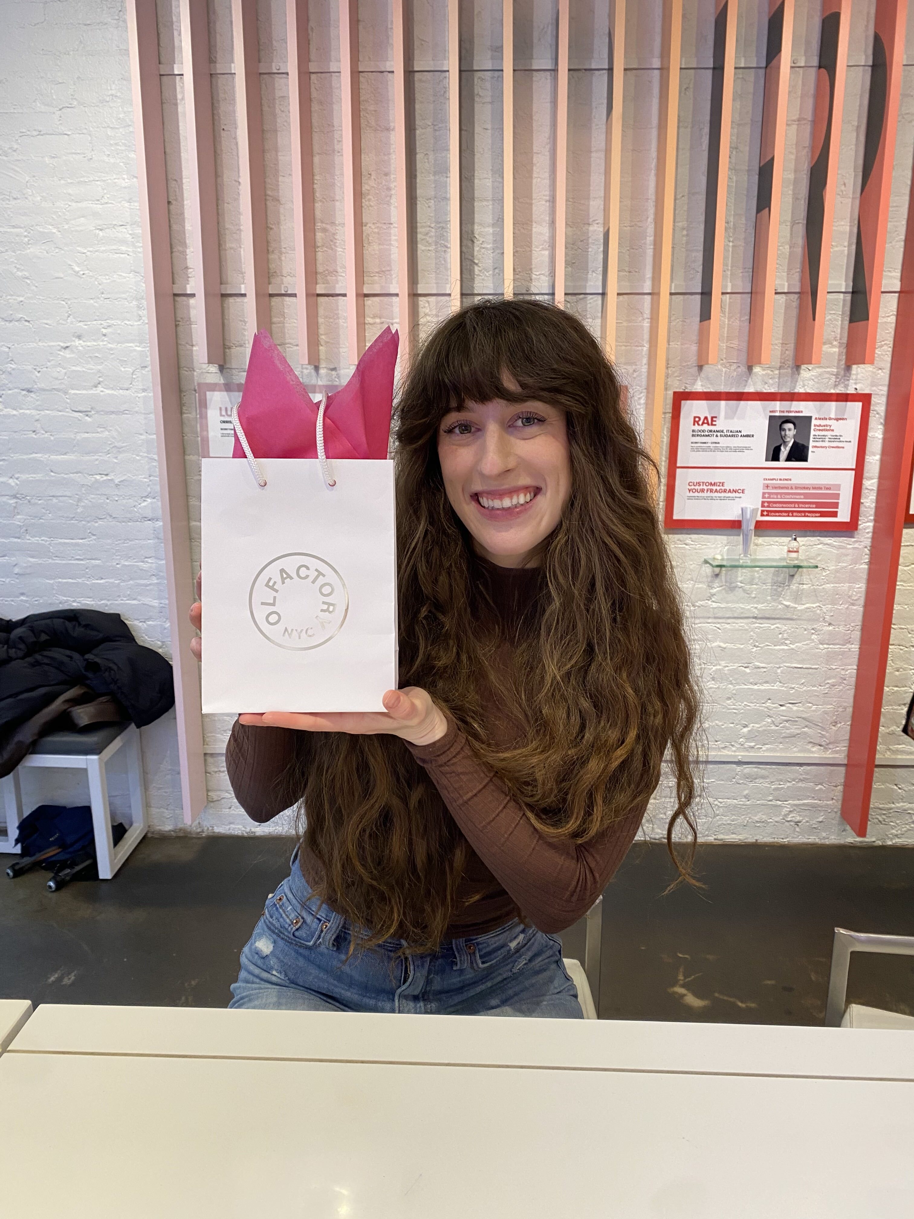 Bella holing a white gift bag from Olfactory, perfume experience in NYC