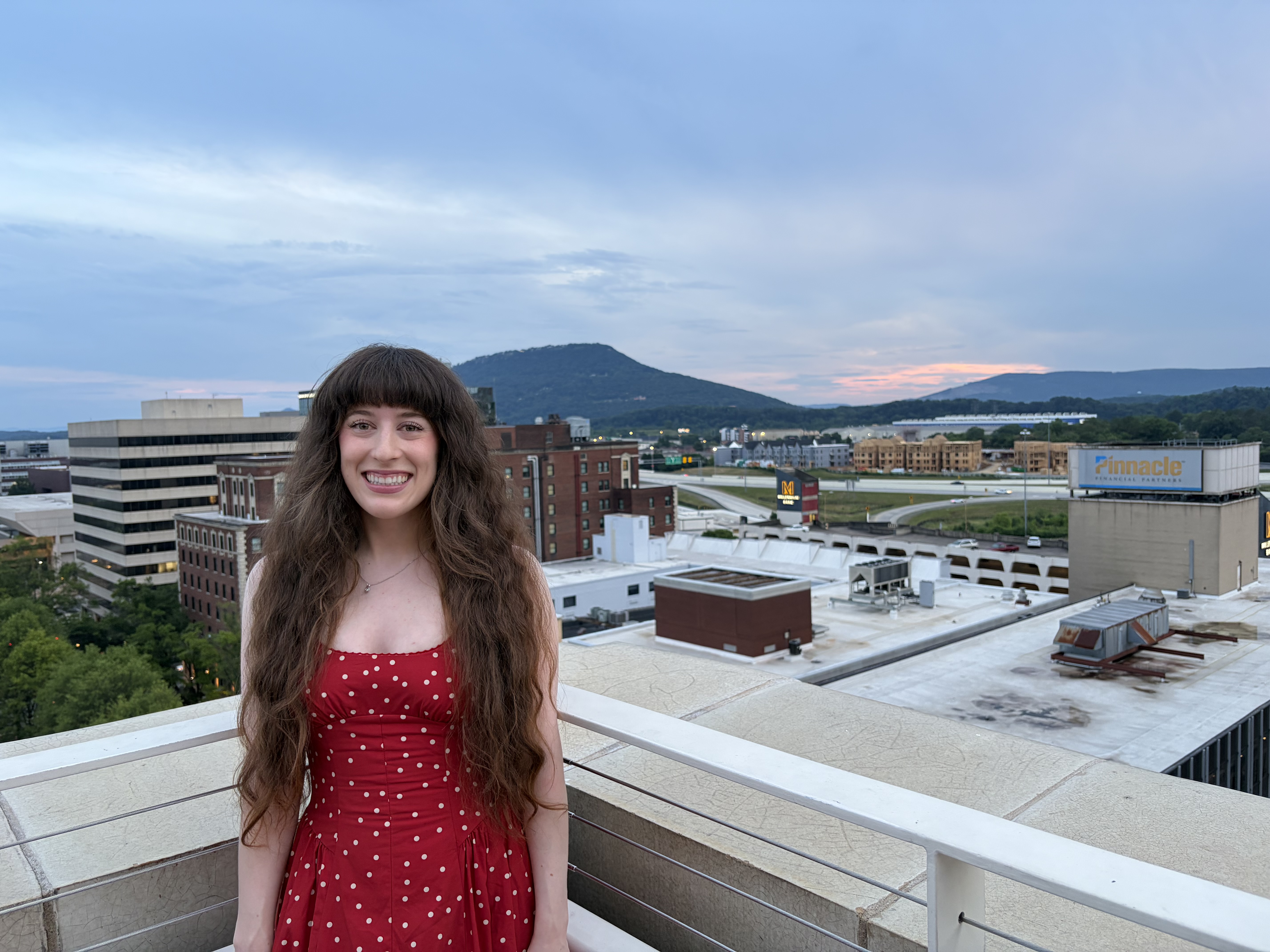 Young woman posing in red polka dot dress in front of the city of Chattanooga at the Waymark rooftop bar. 