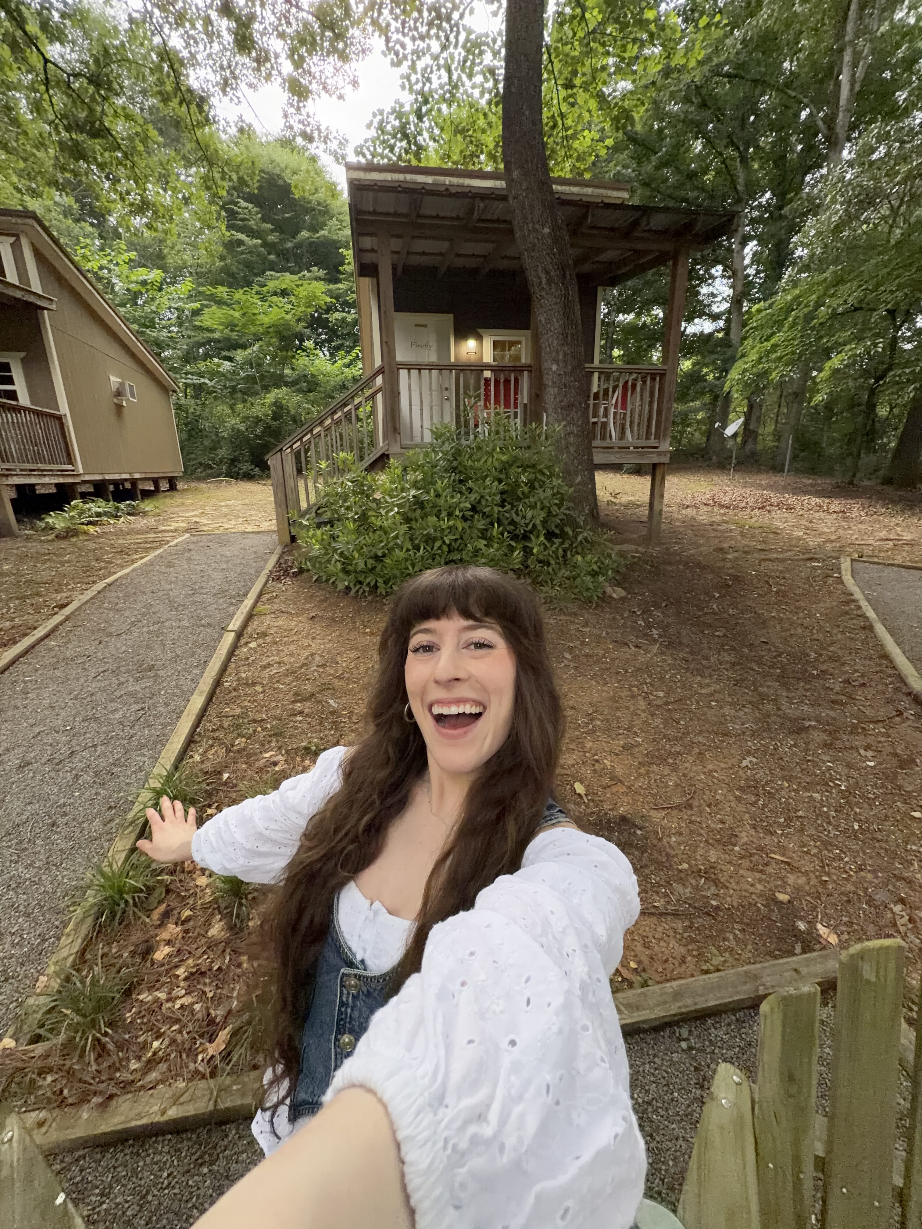 Bella wearing a flow white shirt with jean vest posing and smiling in front of a bungalow at Adventures Unlimited. 