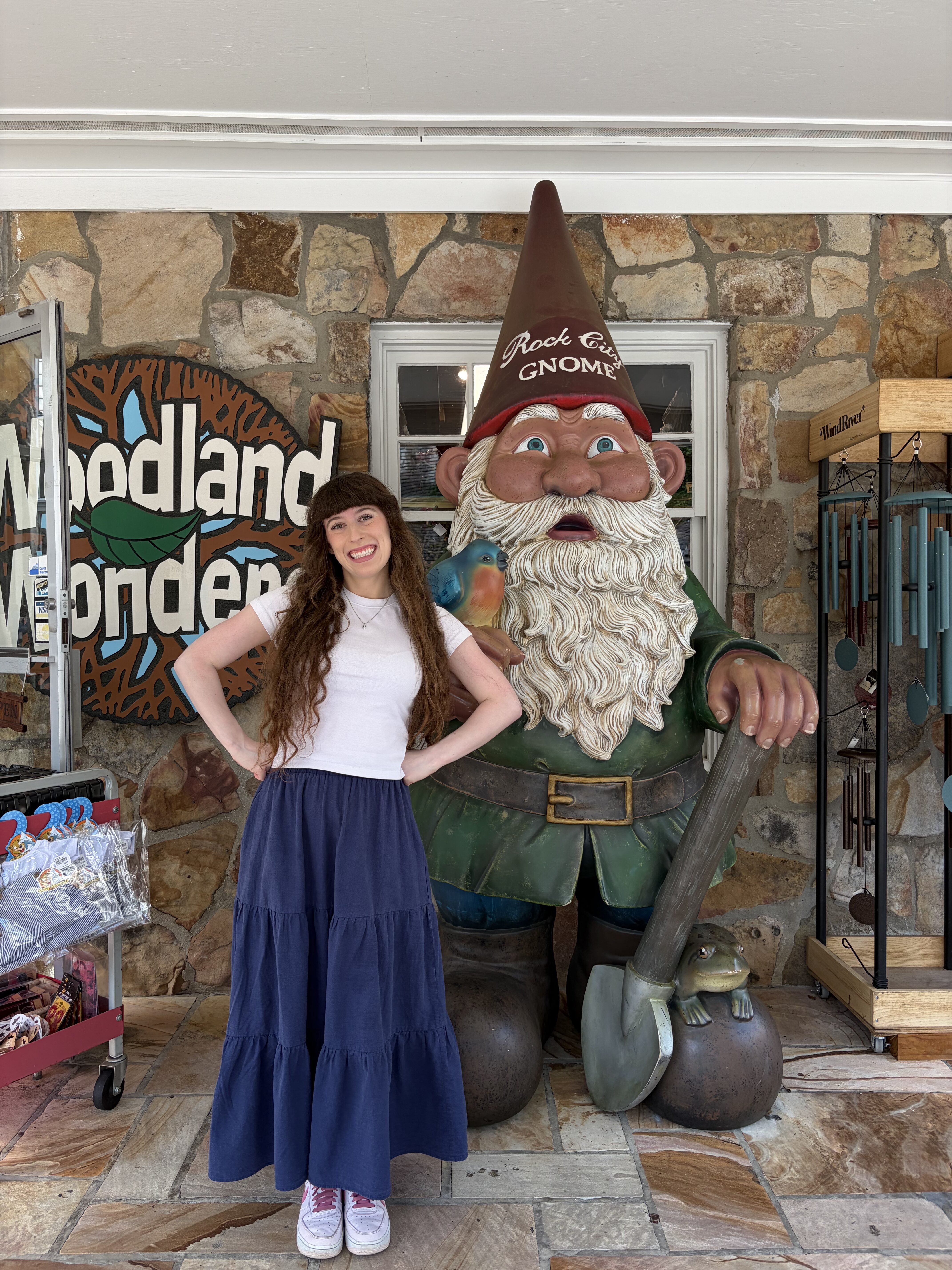 Bella, wearing a white shirt and a dark blue skirt, smiling with a large wooden gnome, Rock City gift shop.