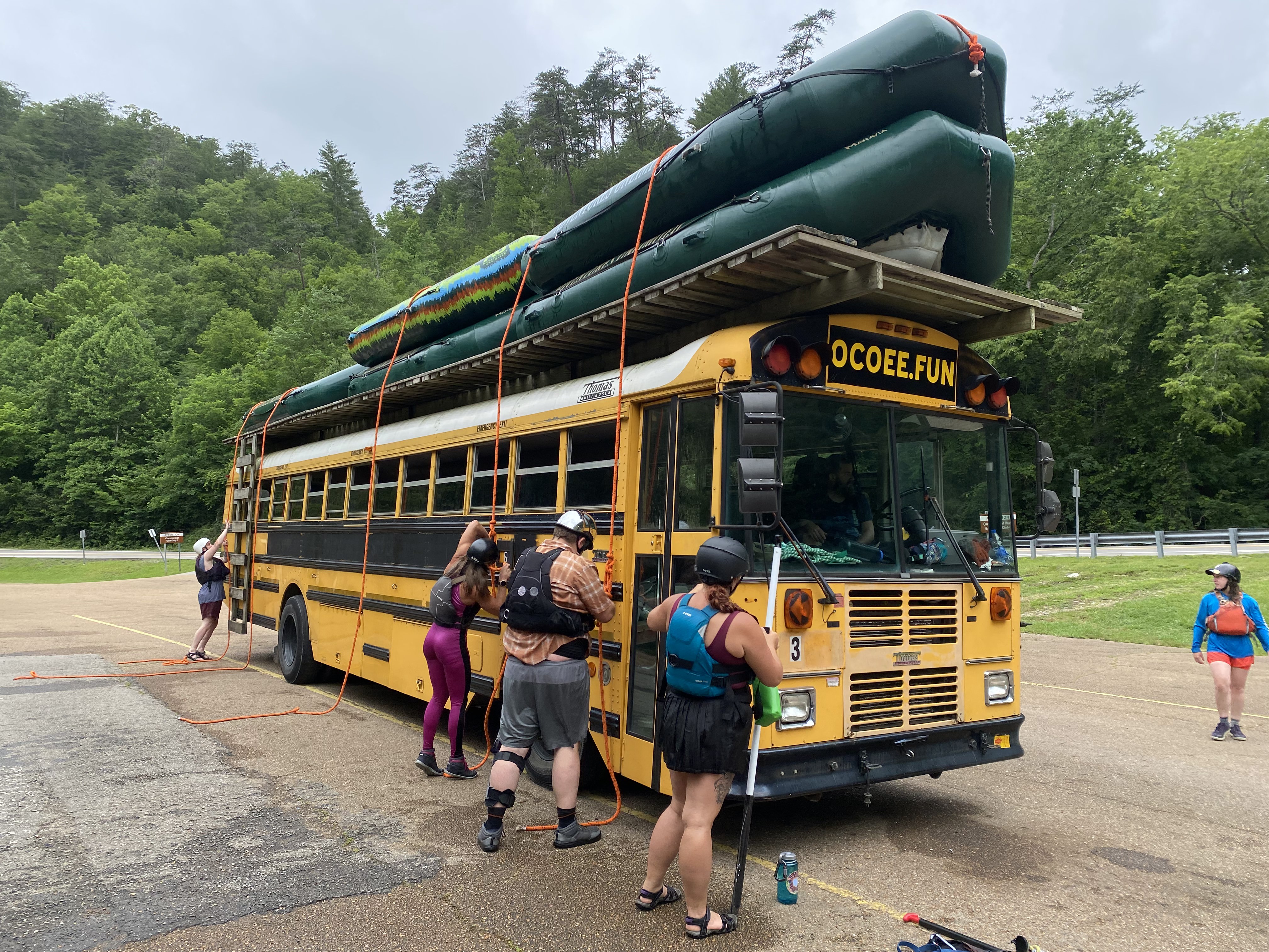 Yellow school bus with green rafts stacked on top.