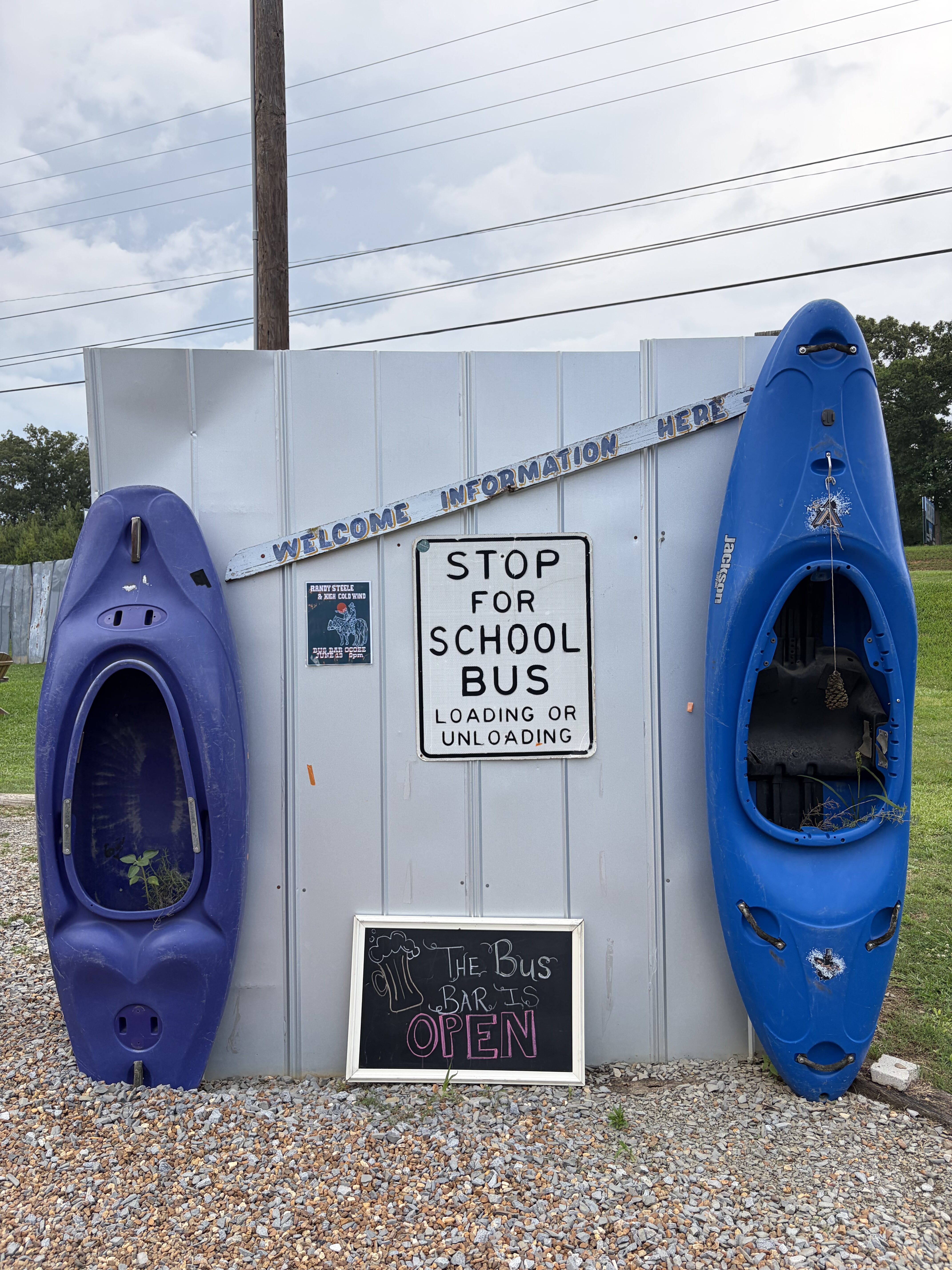 A purple and a blue kayak propped up on a white wall with a sign that says "Stop for School Bus" at Adventures Unlimited.
