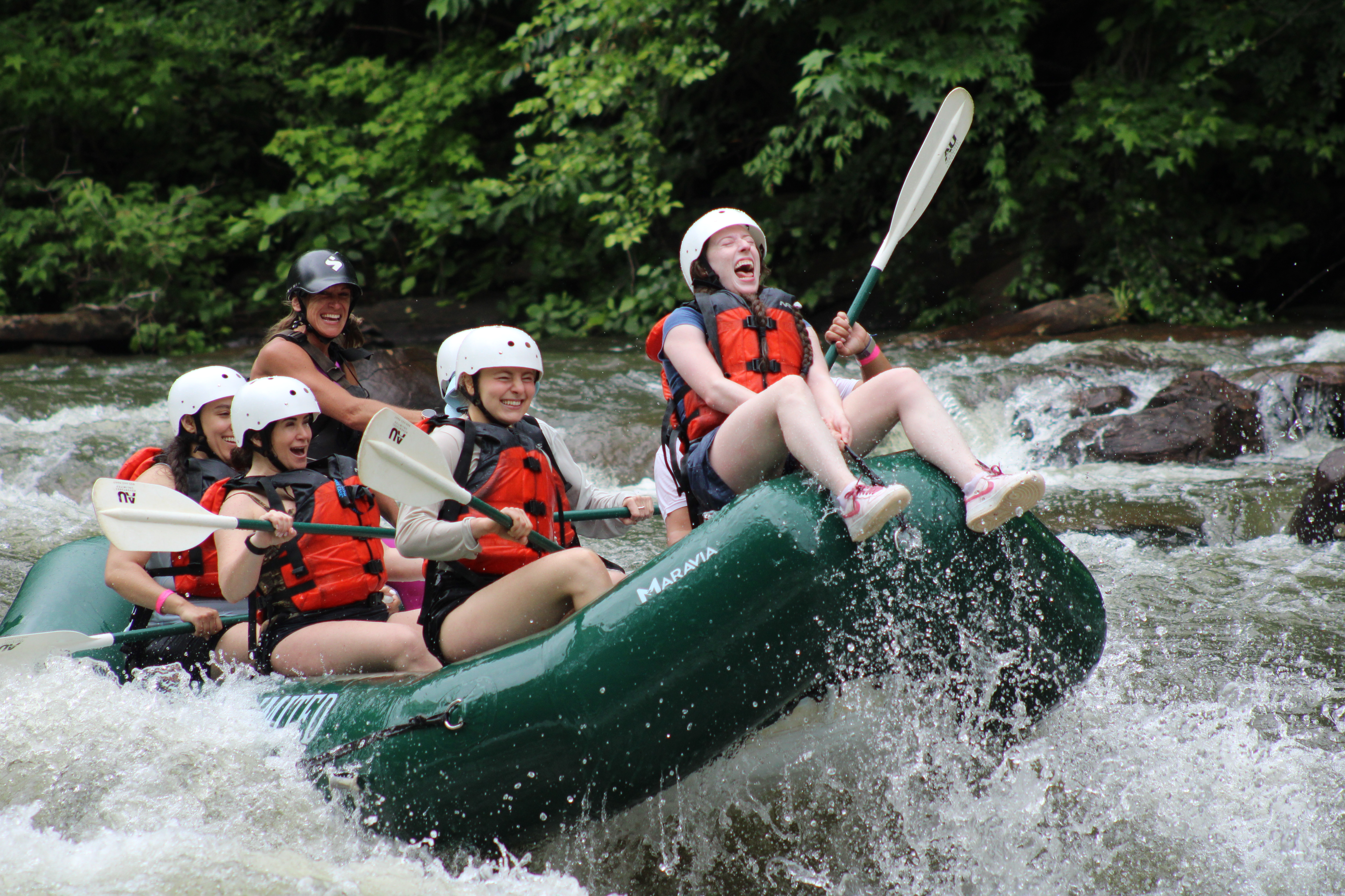 A group of women river rafting on the Ocoee River with one woman screaming while sitting on the front of the boat. 