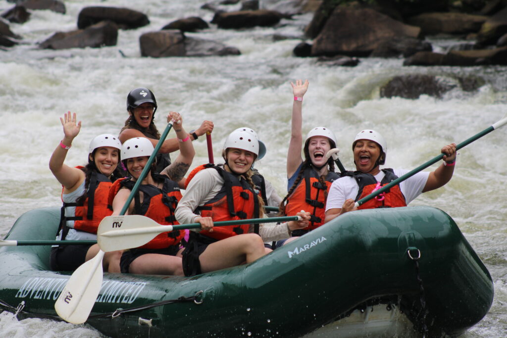 A group of rafters in a green raft on the Ocoee River waving to the camera.