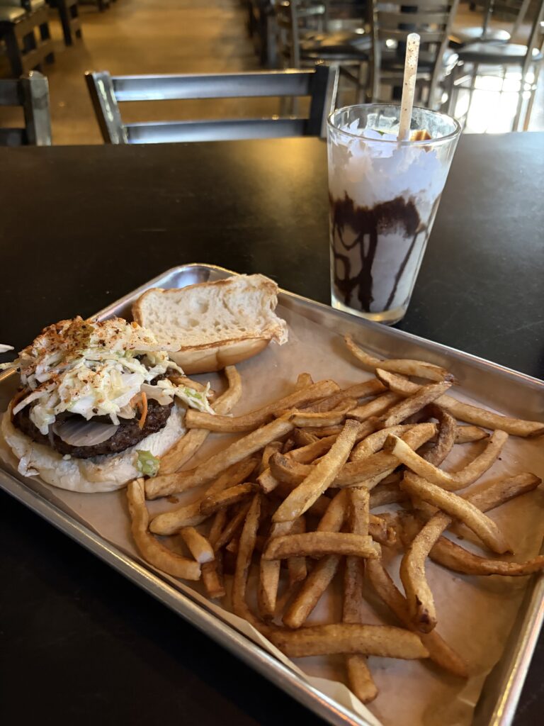 A tray with an open-faced burger, a scattering of french fries and a chocolate milkshake from Urban Shack Chattanooga.