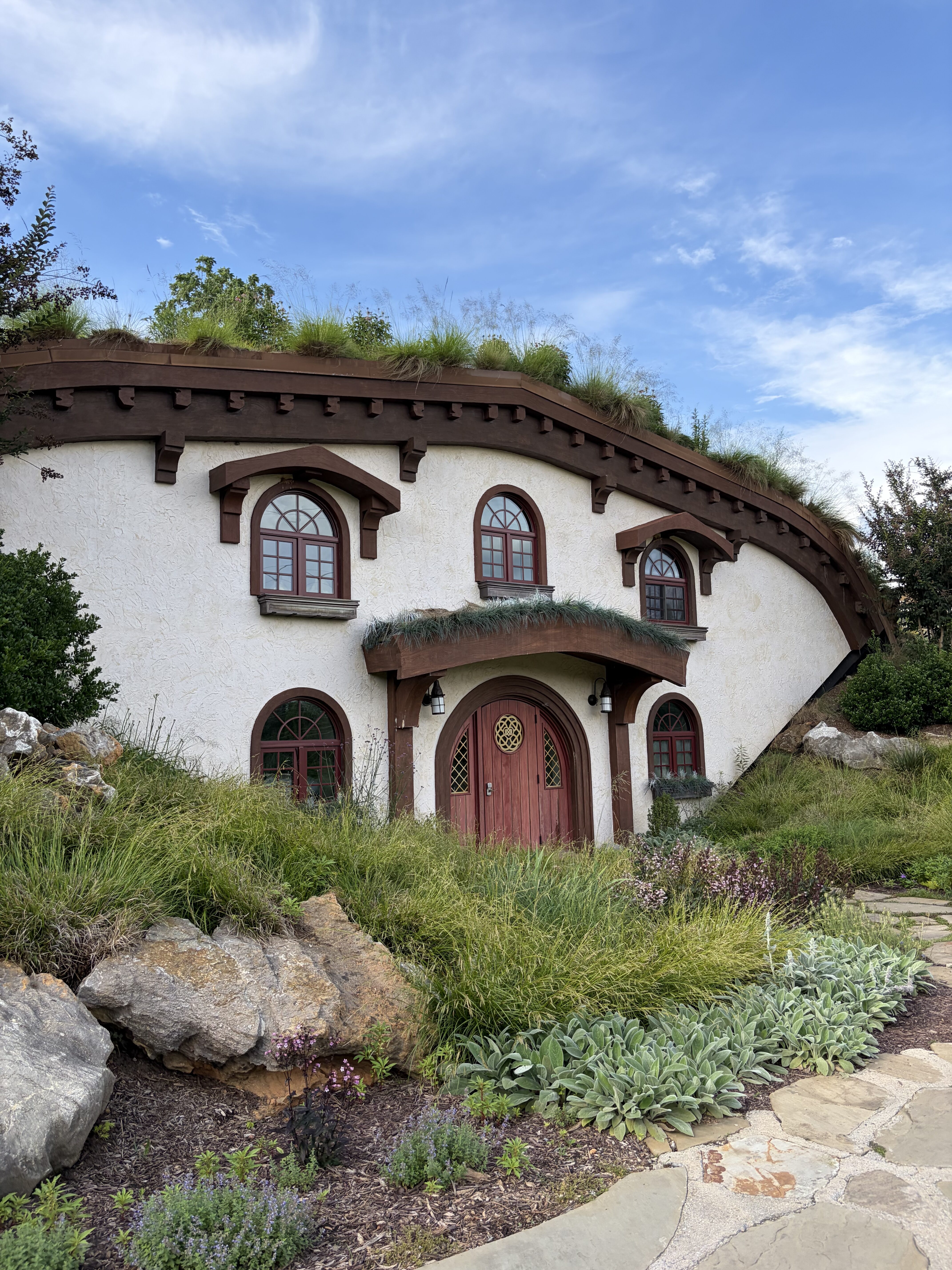 A whimsical white "Hobbit-style" house with a grass roof and a red door. 