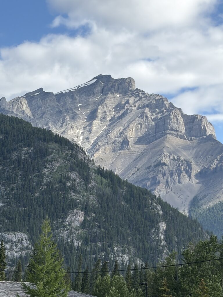 Grey limestone mountain in Banff towering over a pine-covered mountain in front of it.