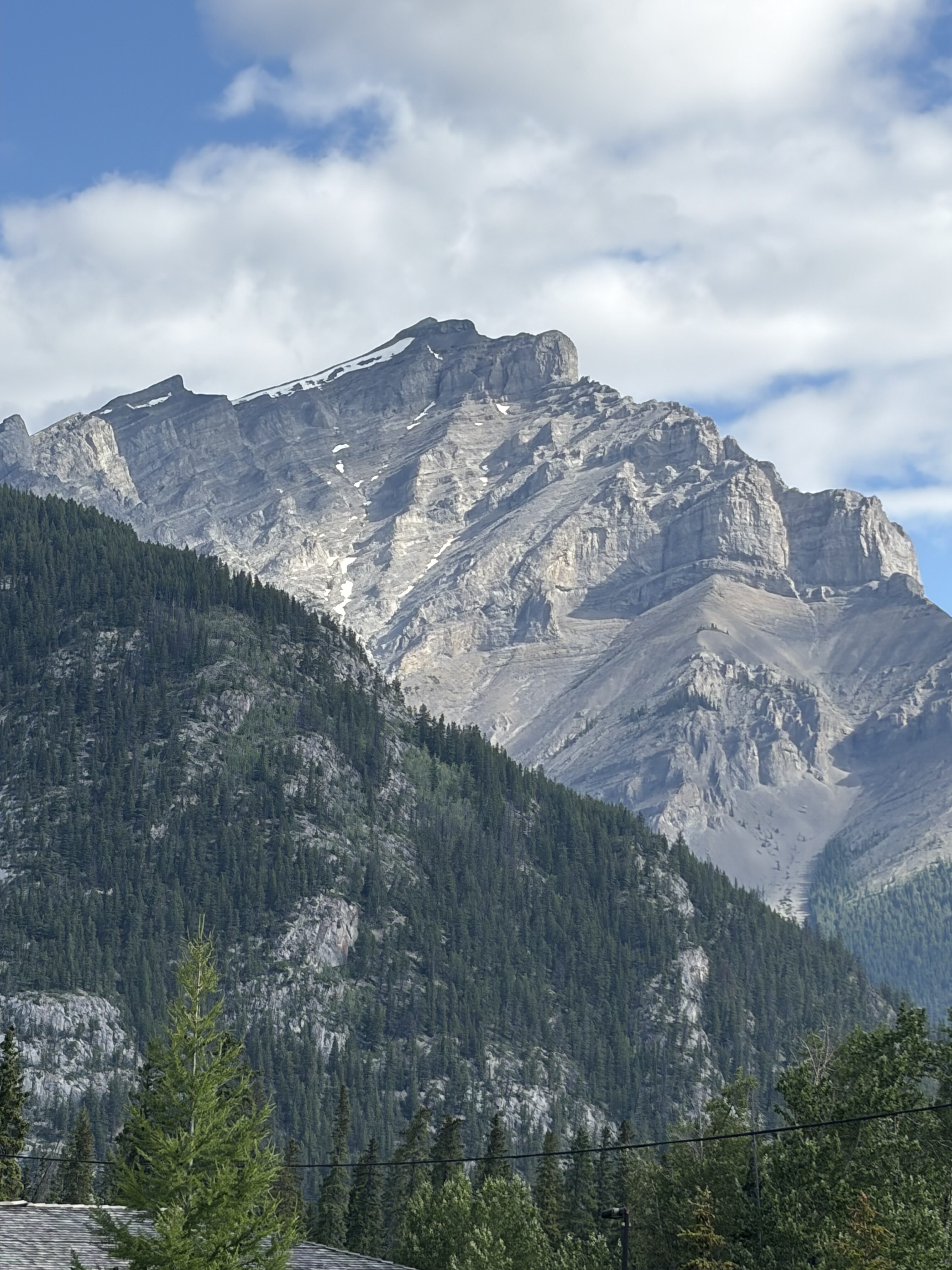 Grey limestone mountain in Banff towering over a pine-covered mountain in front of it.