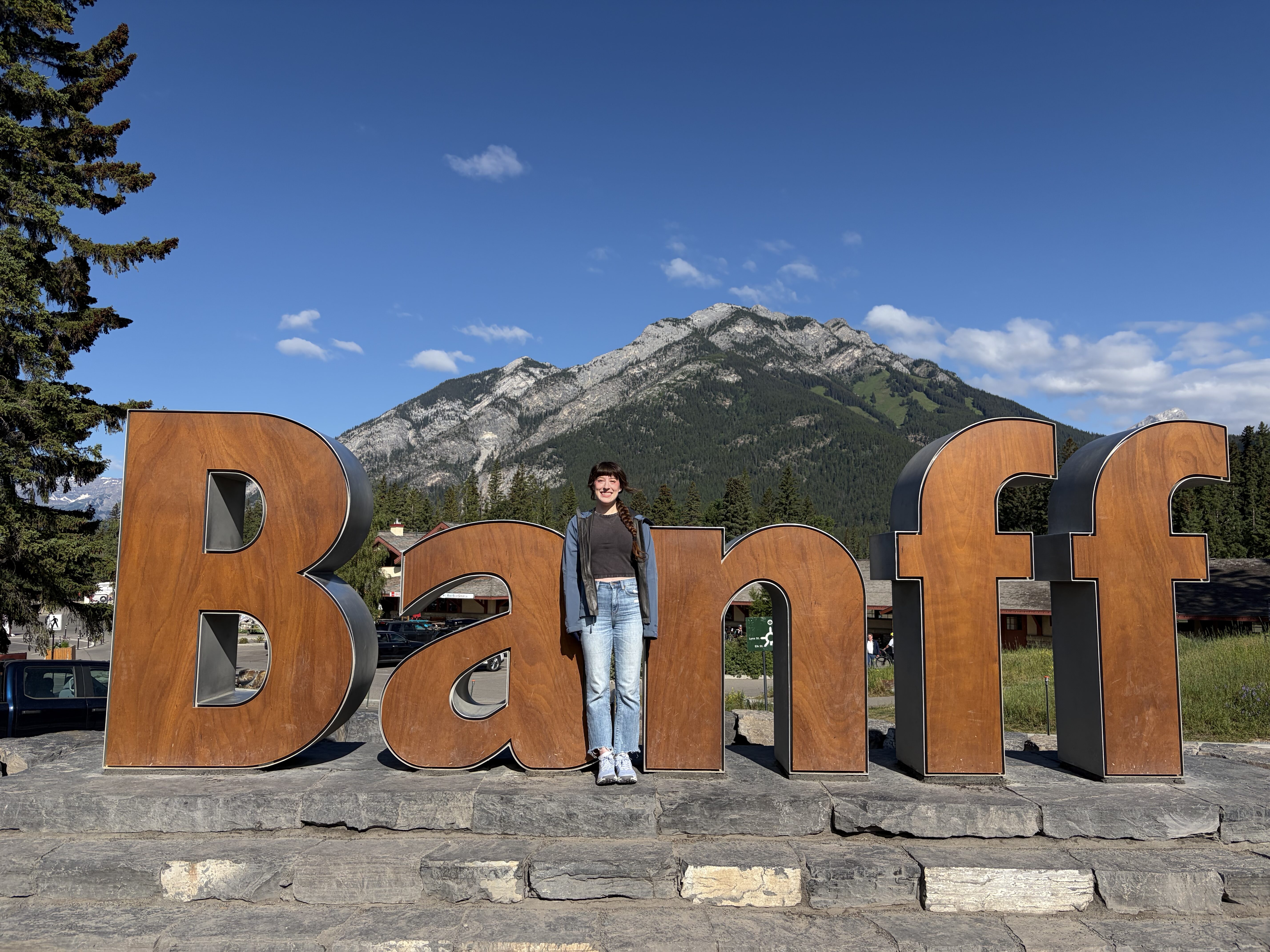 Bella smiling in front of the "Banff" sign, squinting in the sun.