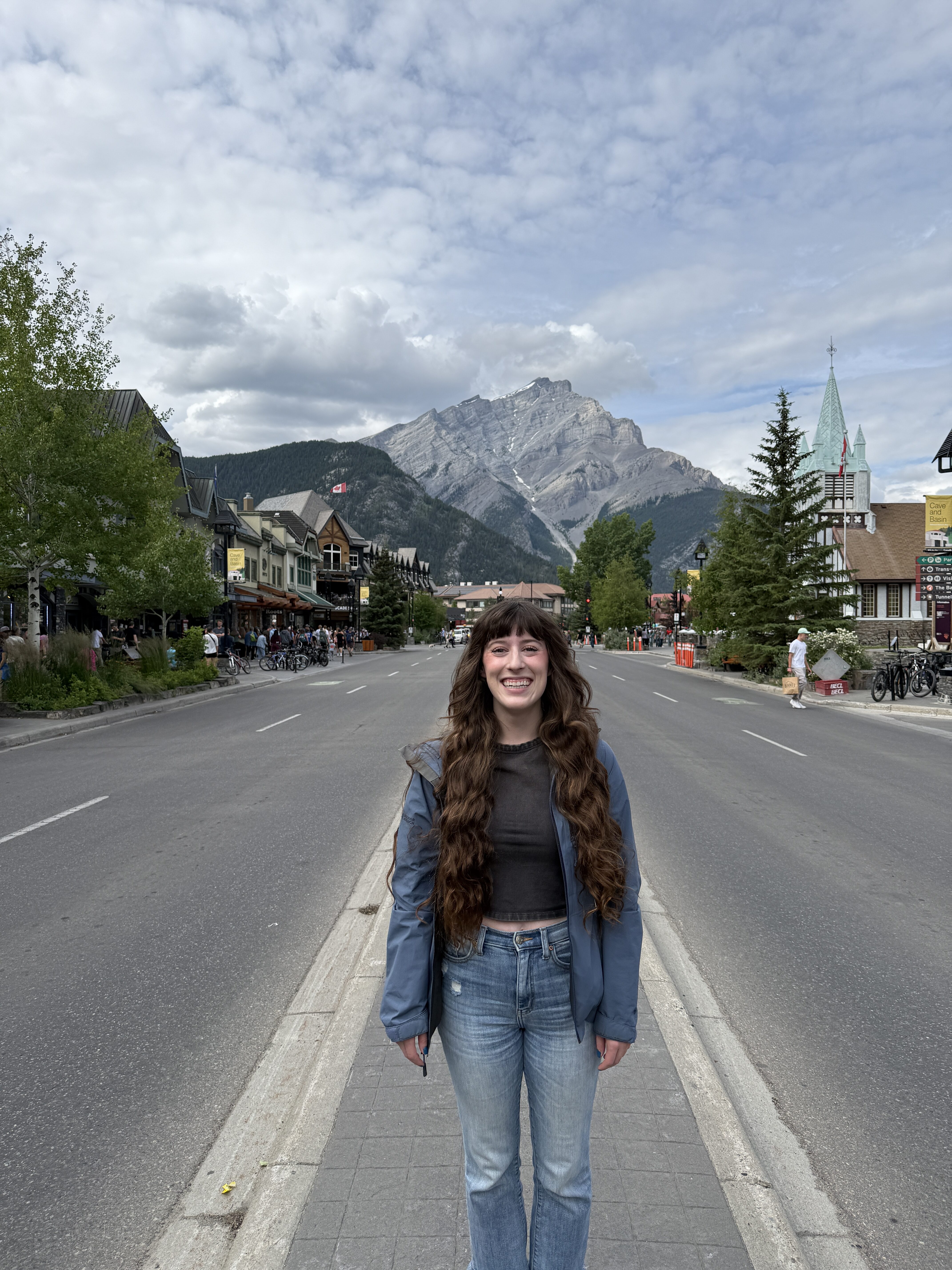 Bella smiling happily in the center of Banff town with Cascade mountain in the background. 