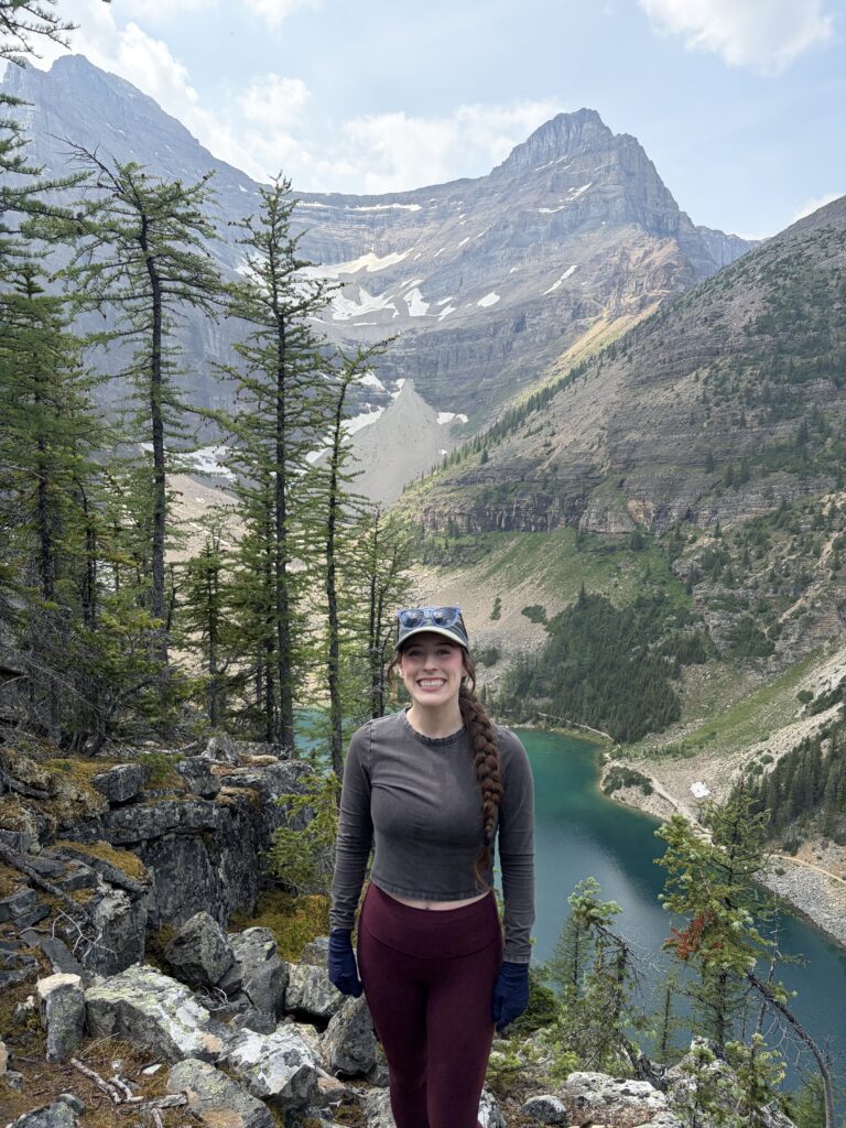 Bella smiling at the top of Big Beehive hike, with views of Lake Agnes and the mountains towering over it. 
