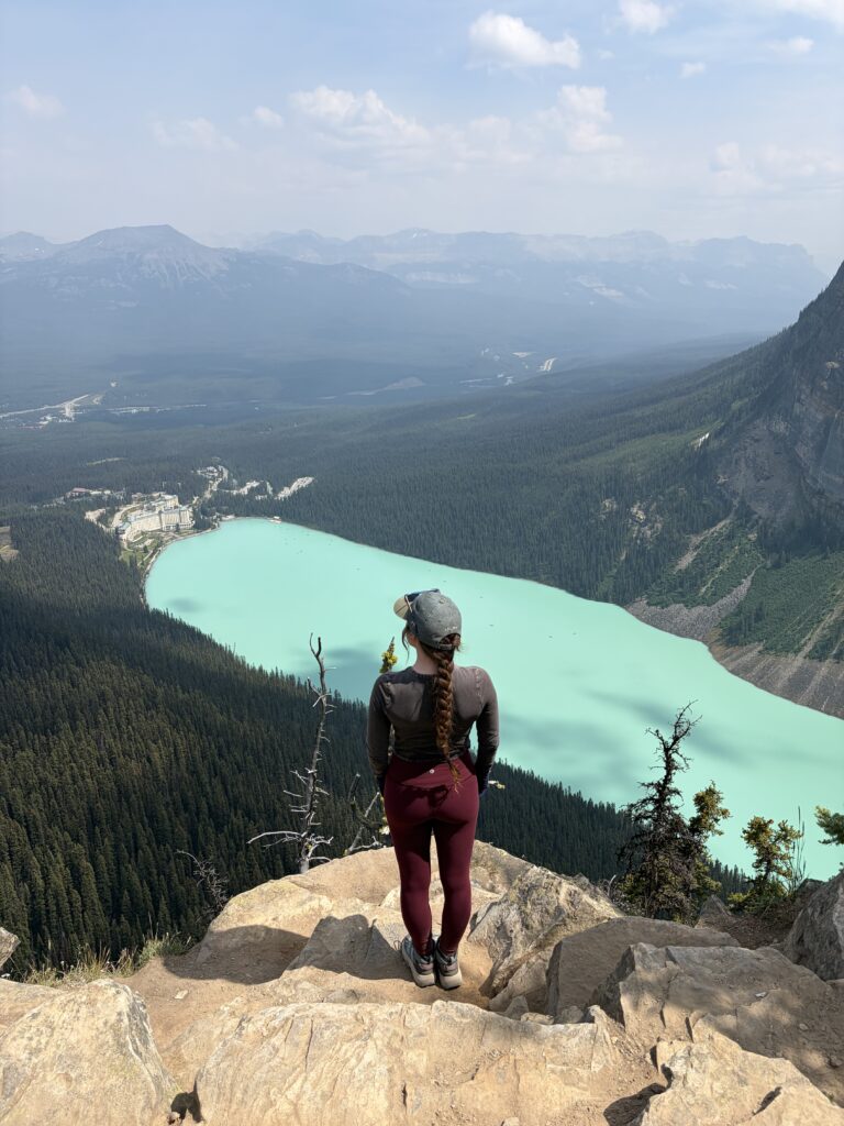 A woman standing on a rock at Big Beehive gazing out upon the aquamarine Lake Louise.