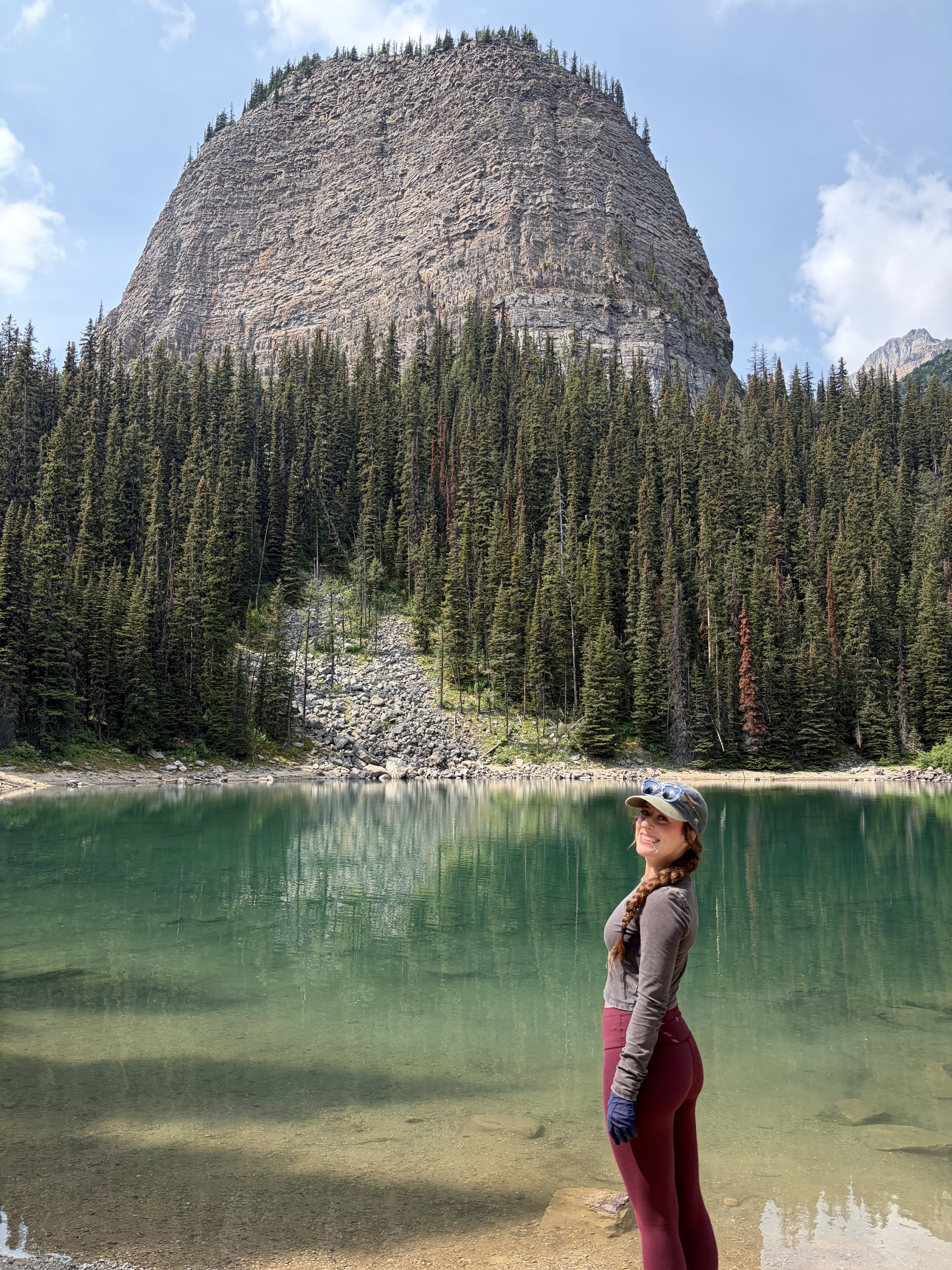 Bella smiling in front of the teal, glassy Mirror Lake with Big Beehive towering over it. 